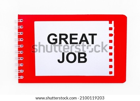 On a white background - a bright red notebook on a spiral. On it is a white sheet of paper with the text GREAT JOB