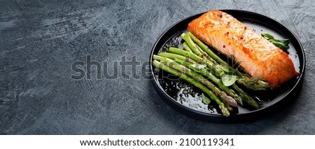 Baked salmon with asparagus on gray background. Mediterranean diet concept. Panorama, copy space Royalty-Free Stock Photo #2100119341