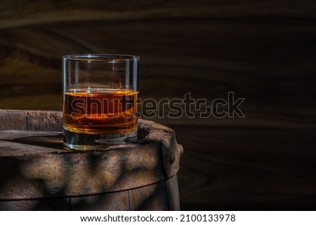 Glass with whiskey, spikelets of wheat, brandy on a vintage background of a rustic oaken barrel. Alcoholic beverage. Still life in the old style.