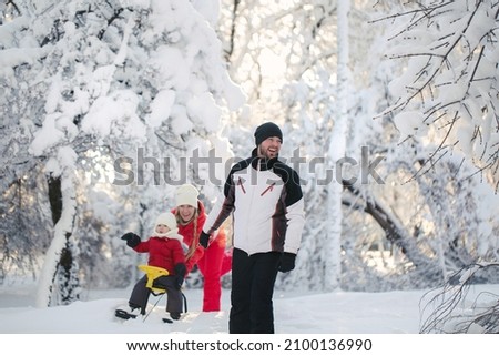 Winter walk: parents sledding with their son. A father pulls a sled with a young son on a snowy day, and a mother pushes.