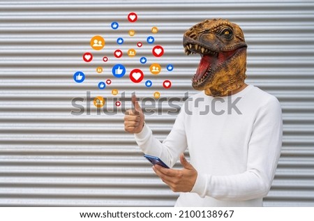 Happy man wearing dinosaur mask using social media app network with mobile phone showing thumb up