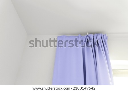 Curtains on window in room with white part of wall, colored in pantone color of 2022 year - Very Peri