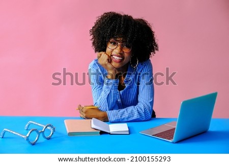 cheerful young businesswoman leaning on hand and smiling at camera at workplace
