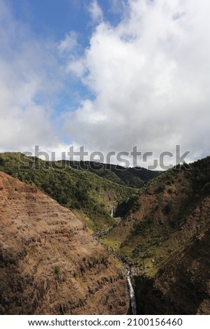 An aerial view of Waimea Canyon with two waterfalls in the distance and with large cumulus clouds in Kauai, Hawaii, USA