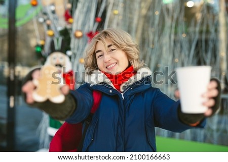 Portrait of a woman with a red scarf. The woman holds coffee and gingerbread in her hands and smiles.