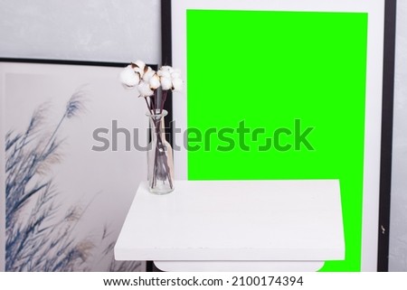 interior picture stands green screen mockup for photoshop replacement of the background in a dark frame picture light interior white table place for an object foreground vase white cotton bouquet