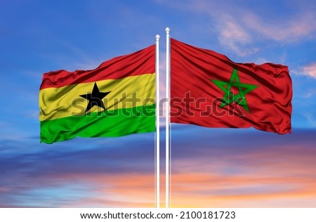 Morocco and Ghana two flags on flagpoles and blue cloudy sky  Royalty-Free Stock Photo #2100181723