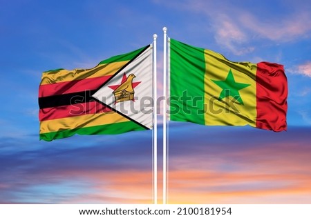 Senegal and Zimbabwe two flags on flagpoles and blue cloudy sky  Royalty-Free Stock Photo #2100181954