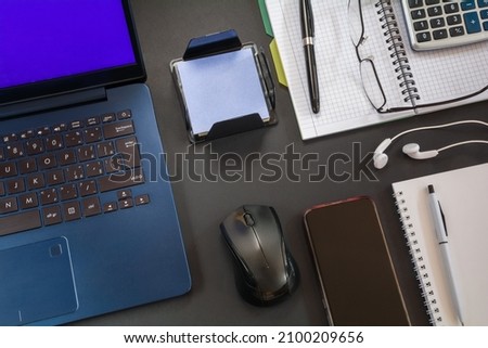 Laptop with mouse, notebook with pen and other accessories on the desktop with a dark surface
