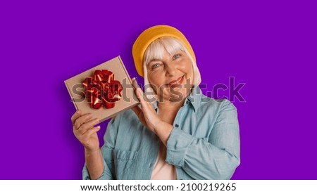 Portrait of attractive romance 50s woman hands holding gift good mood isolated over bright purple color background