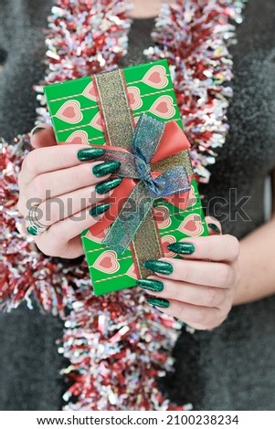 Female hands with long nails and bright green manicure hold a gift box.