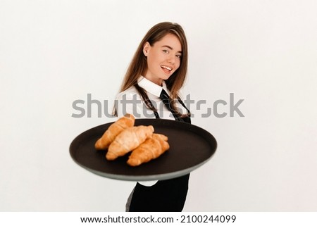 Portrait of elegant waitress in black apron serving customer in a pastry shop, giving croissants