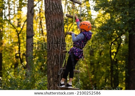 Happy school girl enjoying activity in a climbing adventure park on a autumn day Royalty-Free Stock Photo #2100252586