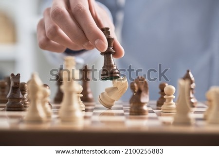 Man's hand holds a chess piece king. A dark colored chess piece. The figure flies. Chess game making a move by a player is an intellectual game.
 Royalty-Free Stock Photo #2100255883