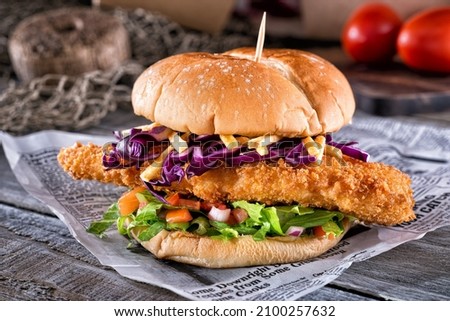 A delicious ultimate fish burger deluxe with breaded fish, lettuce, onion, tomato, red cabbage, mayo, and potato sticks.