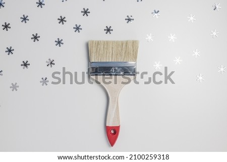 Wooden paint brush on gray with silver snowflakes background. Top view. Winter repairing concept