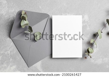 Greeting or invitation card mockup with envelope and dry eucalyptus twig on grey concrete background