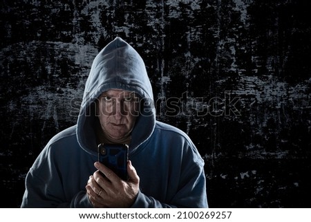 An evil looking man with piercing eyes and a hoodie stands intimidatingly against an ally wall stalking his next victim.     Royalty-Free Stock Photo #2100269257