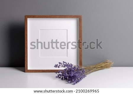Square wooden frame mockup for artwork, photo, print and painting presentation with dry lavender flowers over grey wall.