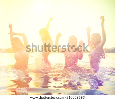 Group of happy teen girls playing in water at the beach on sunset. Beauty and joyful teenager friends having fun, dancing and spraying over summer sunset. Beach party. Sun flare.