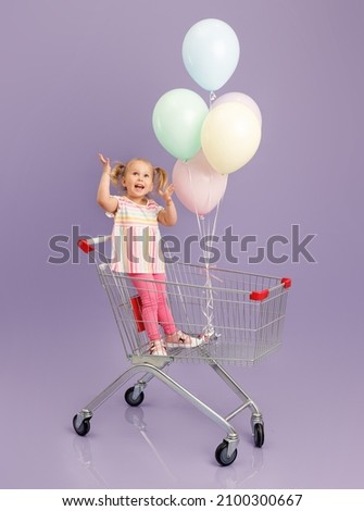 A little girl smiles sitting in a shoping cart with colorfull balloons. Isolated concept image of the shopping with copy space.
