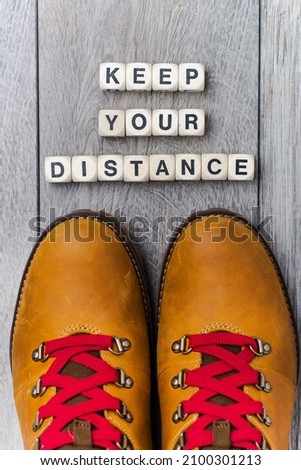 Legs in boots with red laces on the gray floor in front of the inscription - KEEP YOUR DISTANCE.
