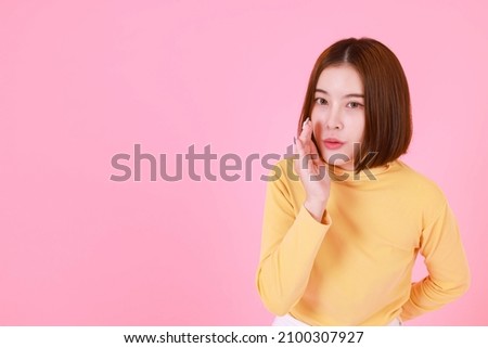 Portrait studio cutout shot of Asian young pretty short hair female model in yellow long sleeve shirt stand smile to look at the camera and pointing finger on pink background.