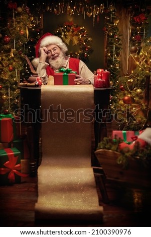 Cheerful smiling Santa Claus thinks about a list of good and naughty children sitting in festively decorated room with a gift box and a long magic scroll in front of him. Christmas fairy tale. 