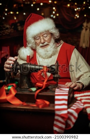 Christmas traditions and fairy tales. Santa Claus sews Christmas stockings in his workshop preparing for giving presents to children. Santa's workshop. 