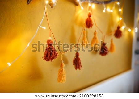 Cozy homemade garland from pompons from threads on the wall in the room, home decor Scandinavian style, mustard and brown, recycling