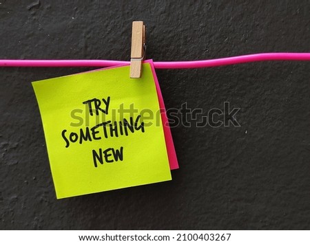Yellow note on gray background with text TRY SOMETHING NEW, to encourage people who are tired of feeling stuck in job or career, to have awareness, inspiration and action around new pathways  Royalty-Free Stock Photo #2100403267