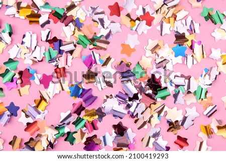 Bright colorful star-shaped confetti sparkles on a pink background, the theme of a holiday and a birthday.
