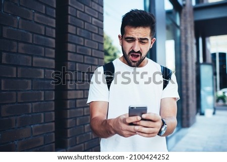 Shocked travel blogger with modern cellphone reading received mail message and amazing, wonder hipster guy with digital smartphone technology feeling impressed during mobile messaging in networks