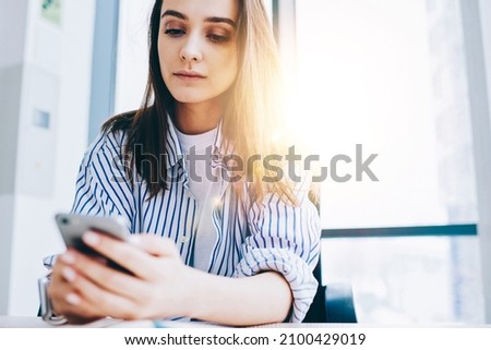 Youthful Caucasian blogger checking smartphone notification for installing application, millennial generation Z with mobile gadget connecting to 4g internet for making online booking and banking