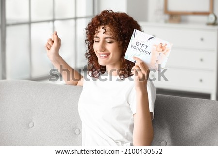 Happy young woman with gift voucher at home