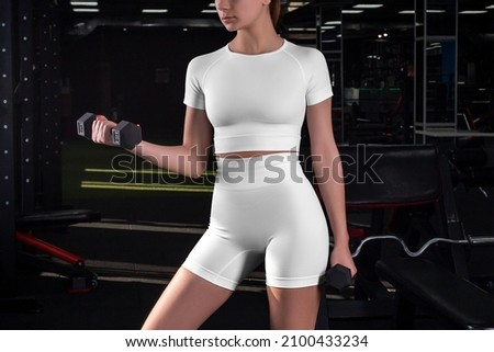 Mockup of white compression underwear, crop top, t-shirt, high shorts on an athlete with dumbbells, on the background of the gym.Empty workout suit template, textured fitness,yoga clothing, for design Royalty-Free Stock Photo #2100433234