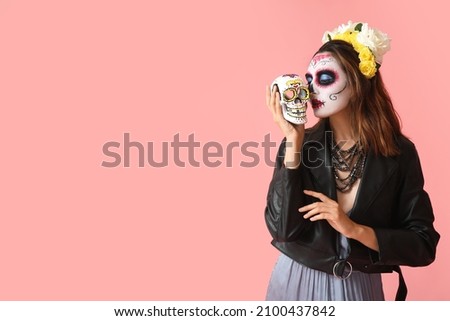 Young woman with painted face and sugar skull for Mexico's Day of the Dead (El Dia de Muertos) on color background