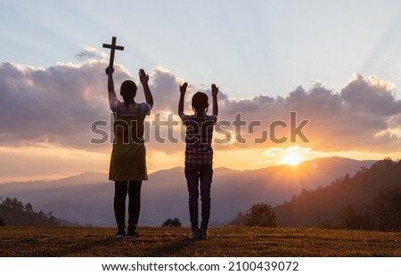 Silhouette of children praying to the GOD while holding a crucifix symbol with bright sunbeam on the mountain