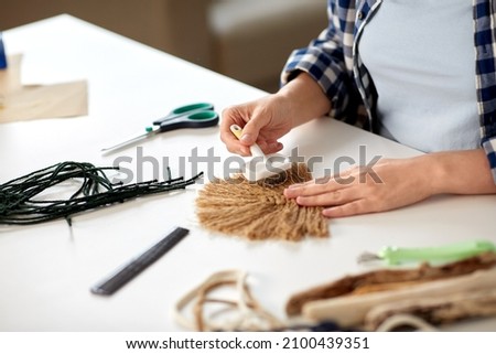 diy, handmade and hobby concept - close up of woman with brush brushing macrame item on table at home Royalty-Free Stock Photo #2100439351