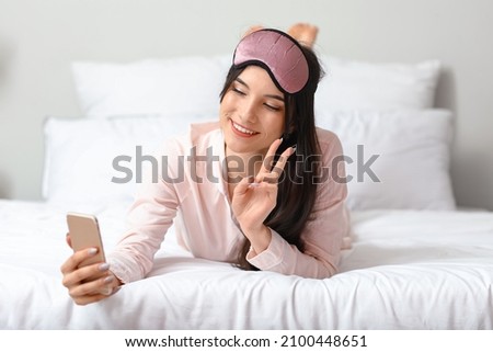 Pretty young woman taking selfie and showing victory gesture in bedroom