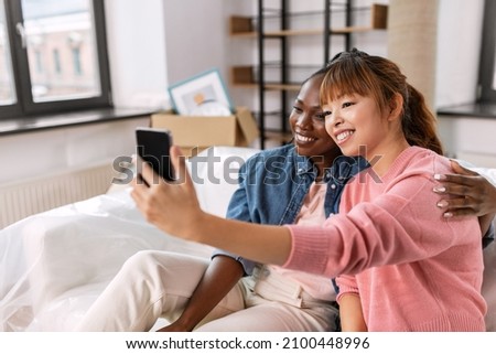 moving, people and real estate concept - happy smiling women with smartphone taking selfie at new home