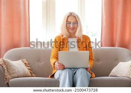 Mature woman in eyeglasses using laptop at home
