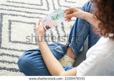 Young woman with gift voucher sitting on sofa at home