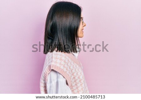 Young brunette woman wearing elegant sweater and glasses looking to side, relax profile pose with natural face with confident smile. 