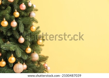 Beautiful Christmas tree with decor on yellow background, closeup