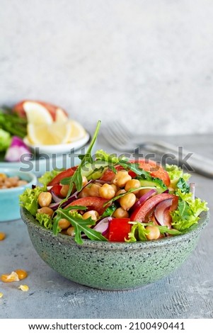 Healthy Vegetarian Chickpea Salad in a bowl with vegetables, herbs and dressing on a blue background. Healthy food concept, A dish of oriental cuisine. Royalty-Free Stock Photo #2100490441