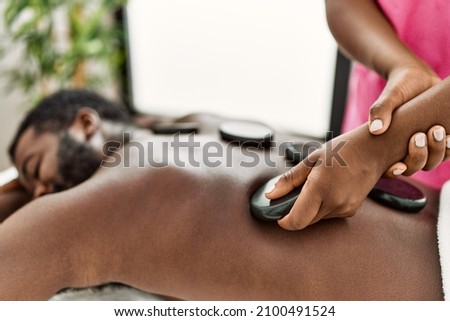 African american man reciving back massage with black stones at beauty center. Royalty-Free Stock Photo #2100491524