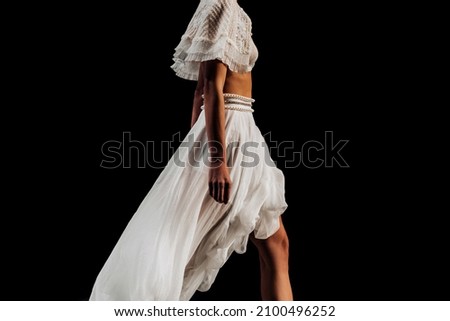 Cropped figure of a fashionable model walking the catwalk in a white designer outfit on black background. Details from Fashion Week