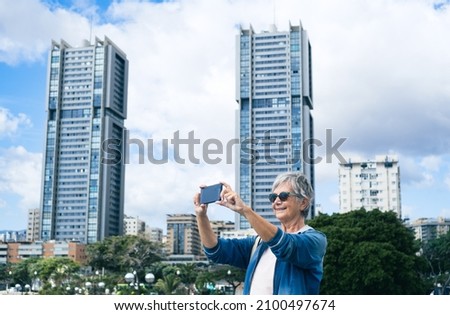 Senior woman with short hair visiting and traveling in Santa Cruz de Tenerife using the phone to take pictures
