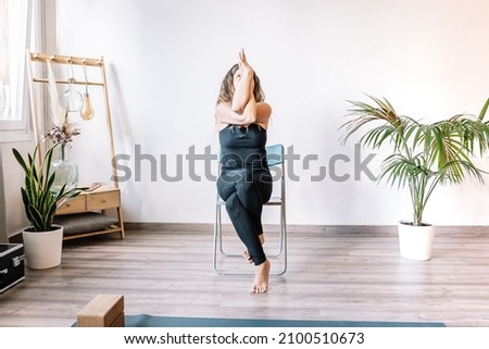 Woman doing Eagle pose on chair Royalty-Free Stock Photo #2100510673